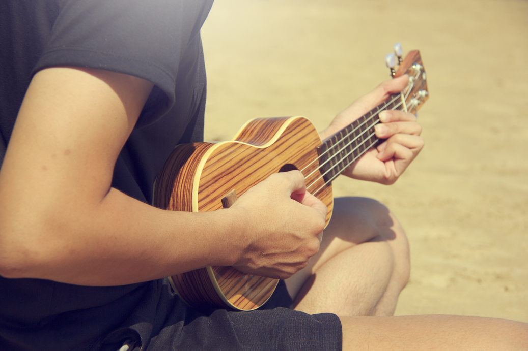 A man playing ukulele on the sandy beach in close up view. travel concept